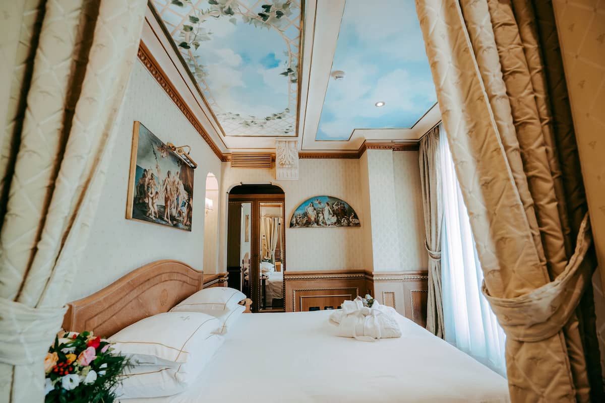 Ein Hotelzimmer mit einem großen Bett, einem Deckenfresko und Blick auf den Flur.