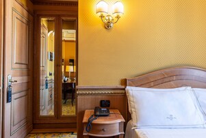 Una camera d'albergo con una porta in legno, un comodino con un telefono, una lampada e un letto con lenzuola bianche.
