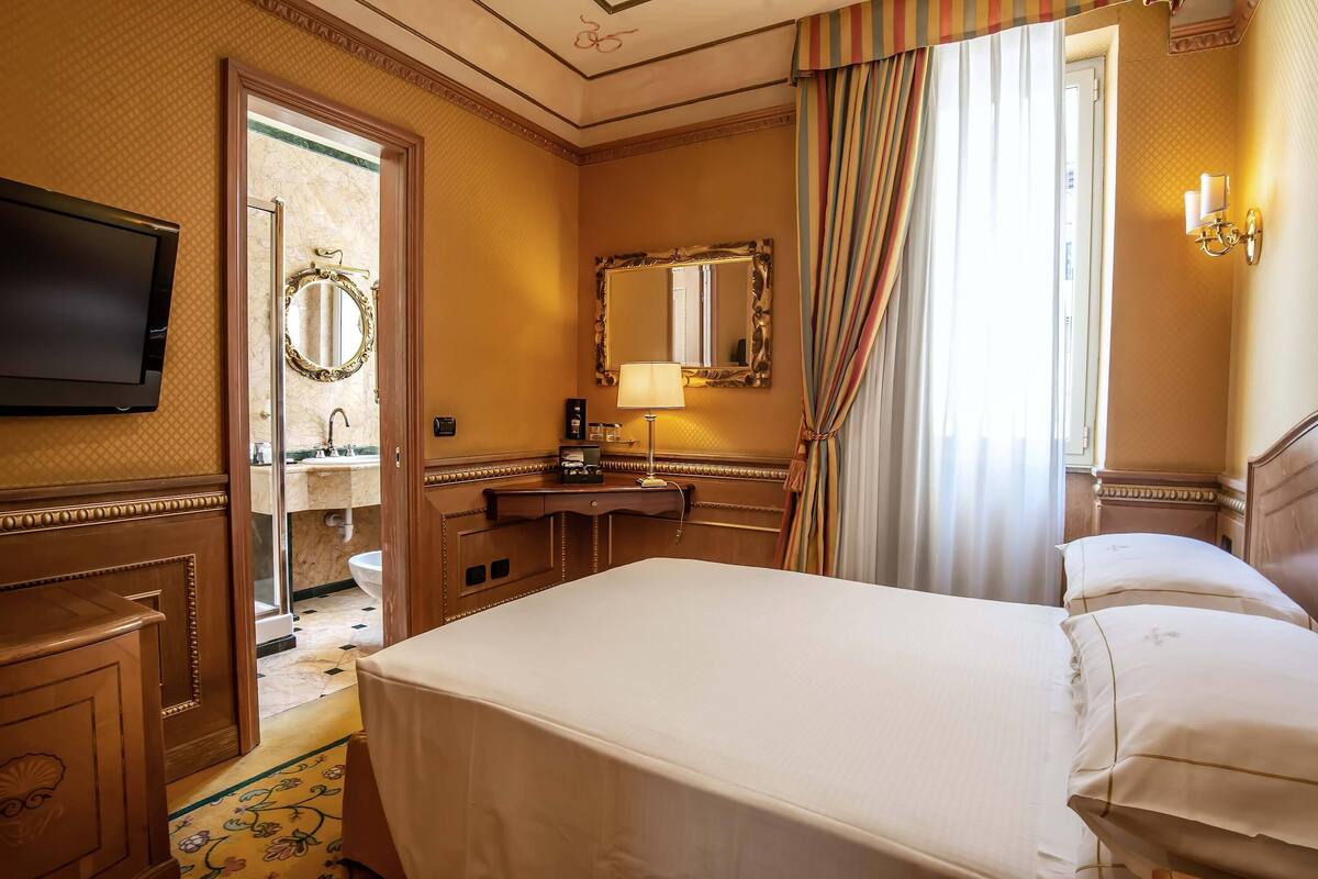 Ein Hotelzimmer mit einem Bett, einem Schreibtisch, einem Spiegel, einem Fernseher und einem durch eine offene Tür einsehbaren Badezimmer.