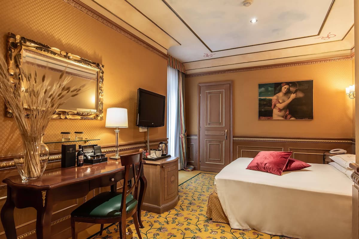 Ein Hotelzimmer mit Bett, Schreibtisch mit Stuhl, Fernseher, einem Bild an der Wand und einer Tür.