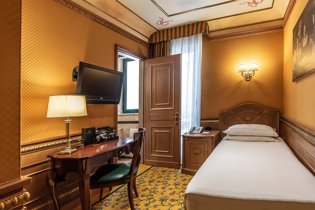 Ein Hotelzimmer mit Bett, Schreibtisch mit Lampe, Fernseher und Telefon.
