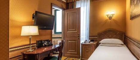 A hotel room with a bed, a desk with a lamp, a television, and a telephone.