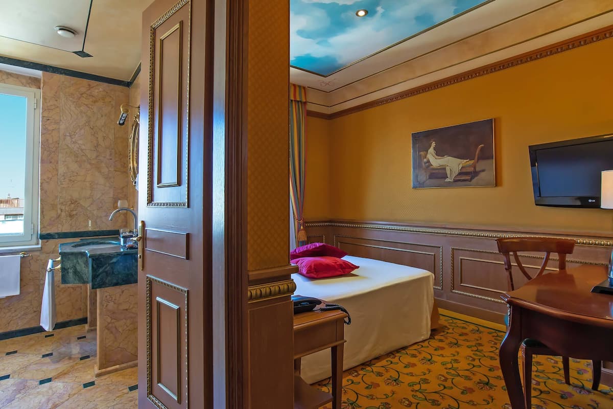 Ein Hotelzimmer mit Marmorbad, einem Bett mit weißer Bettdecke und roten Kissen, einem Bild an der Wand und einem Fernseher.