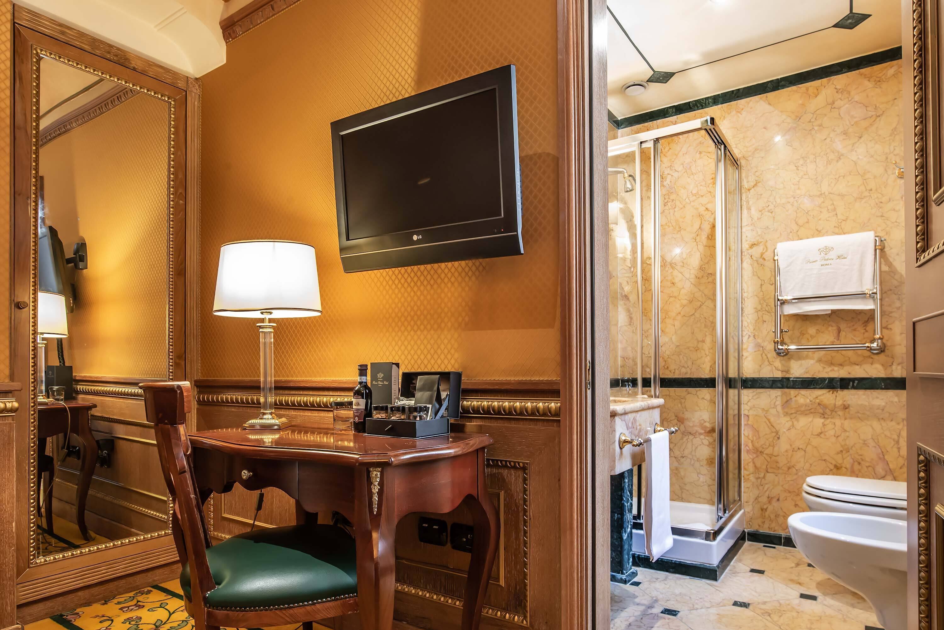 Habitación de hotel con escritorio de madera, una silla, televisor, espejo, ducha y retrete.