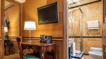 Habitación de hotel con escritorio de madera, una silla, televisor, espejo, ducha y retrete.