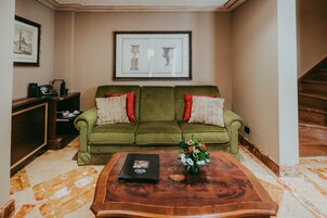 A green sofa with red and white pillows, a framed picture above it, and a wooden coffee table with a book and flowers.