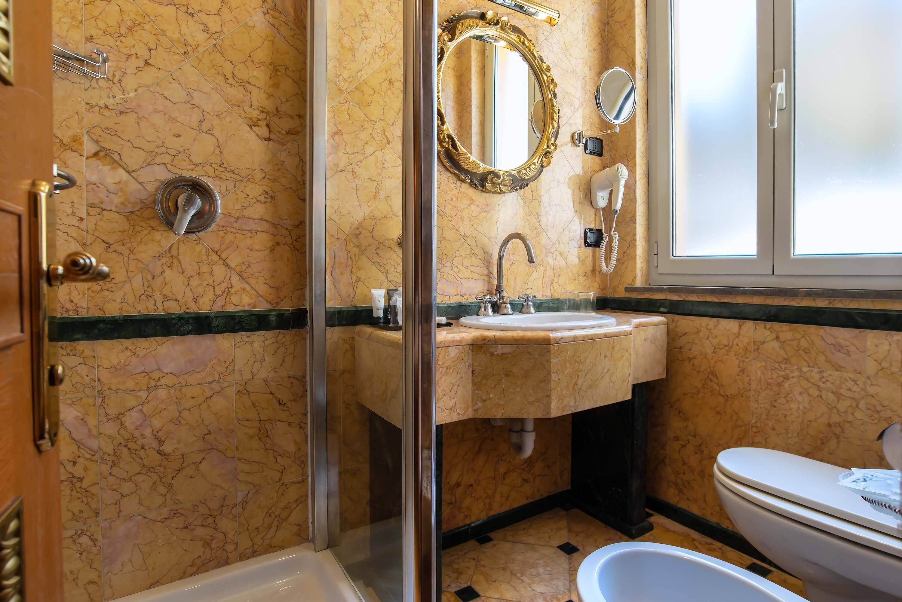 Un baño con ducha envuelta en vidrio, lavamanos con tocador, inodoro y espejo con marco decorativo.