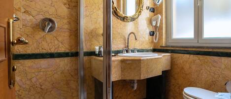 A bathroom with a glass-enclosed shower, a sink with a vanity, a toilet, and a mirror with an ornate frame.