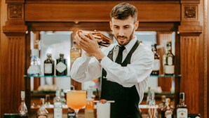 A bartender at a bar with shelves of liquor bottles in the background. - River Palace Hotel (Rome)