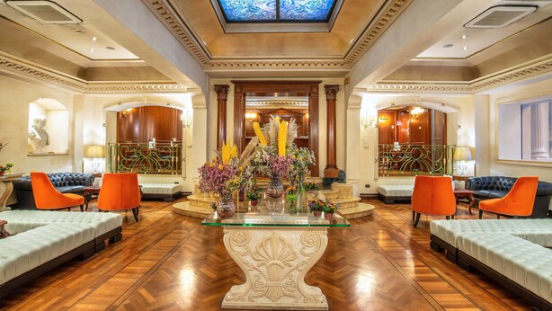 A spacious lobby with a central glass-top table, flanked by sofas and chairs, and a decorative floral arrangement. - River Palace Hotel (Rome)