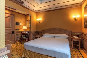 Una camera d'albergo con un letto grande, una scrivania con una sedia, un tavolino e due lampade a parete.