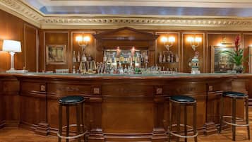 Una zona de bar con mostrador de madera, varios taburetes y una amplia variedad de botellas.