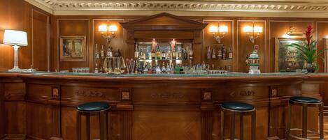 Una zona de bar con mostrador de madera, varios taburetes y una amplia variedad de botellas.