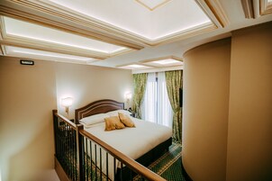 Una camera d'albergo con un letto grande, una testiera in legno, un comodino, una lampada e vista all'esterno attraverso delle tende.