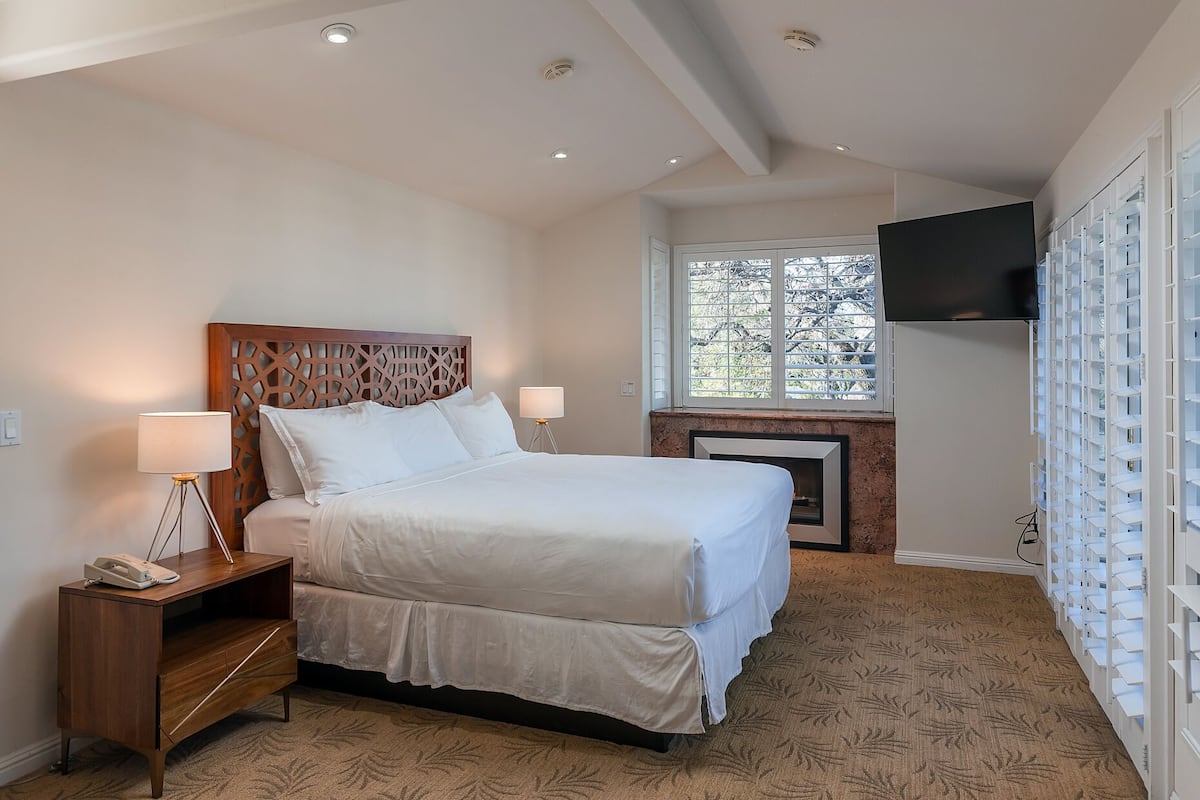 Une chambre à coucher bien aménagée, avec un grand lit, des lampes de chevet, un bureau avec un téléphone, une cheminée et un téléviseur fixé au mur.