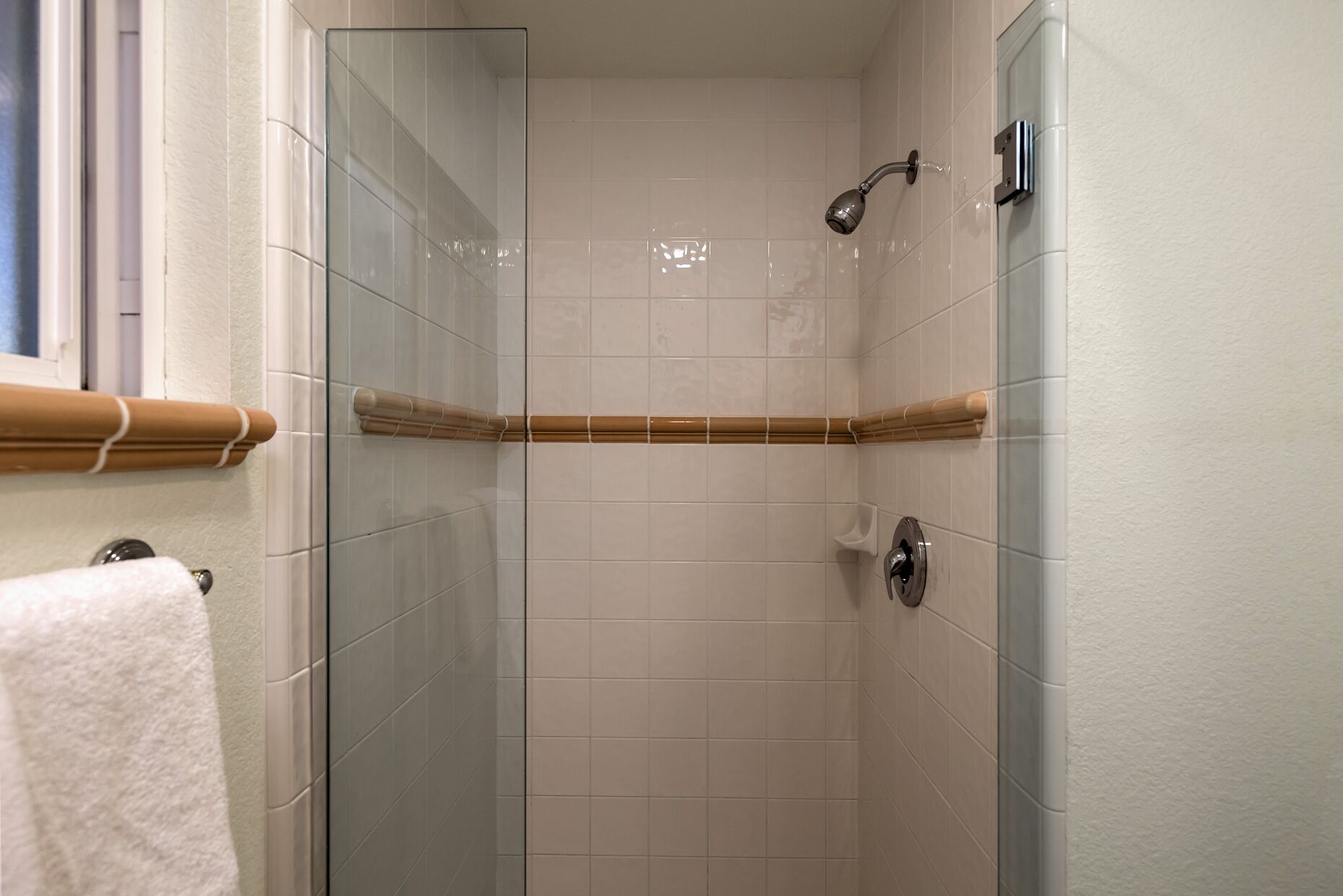 A glass-enclosed shower with a bamboo towel holder, white tiled walls, and a visible showerhead.