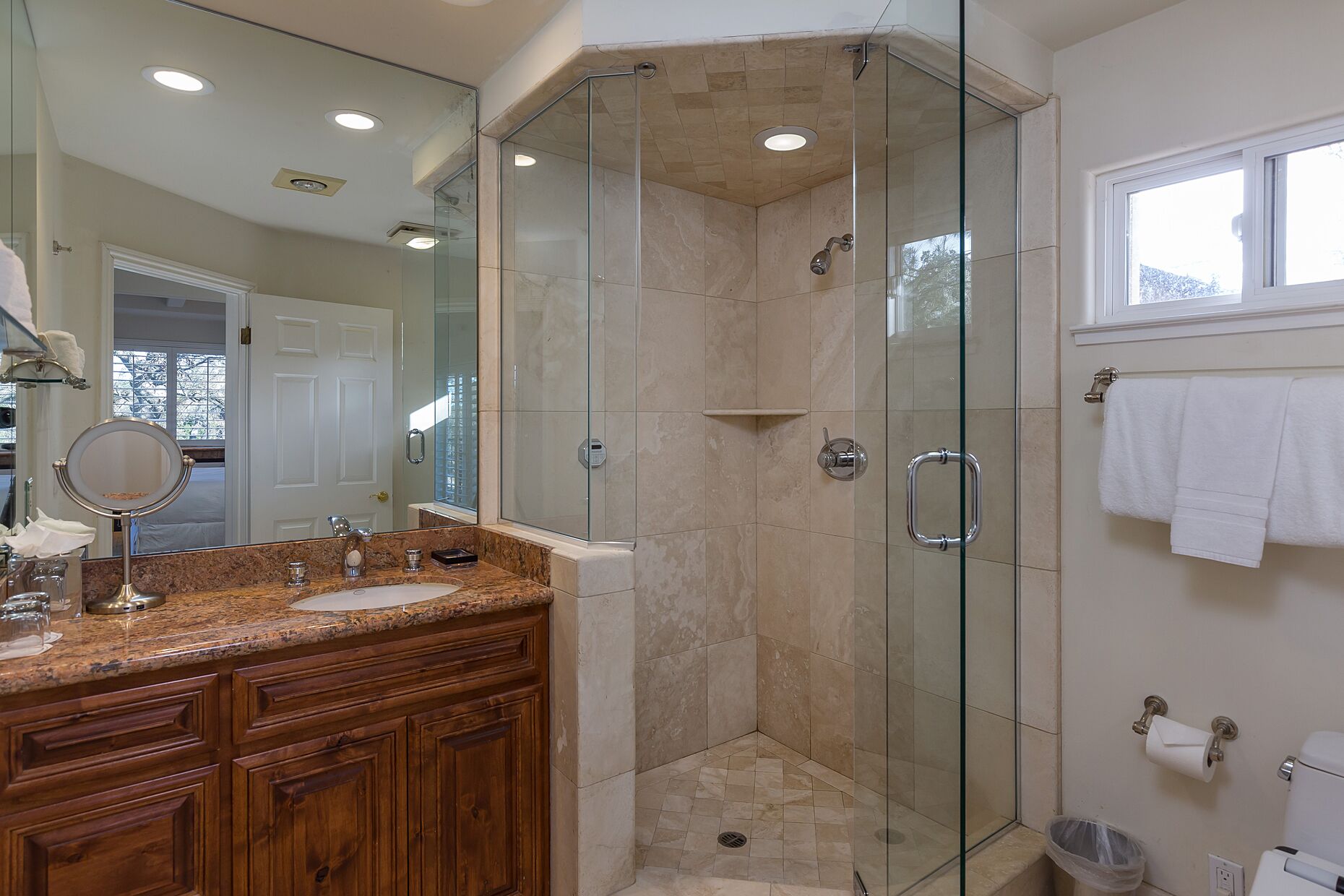 Un baño moderno con ducha de vidrio, tocador de granito y un espejo grande.