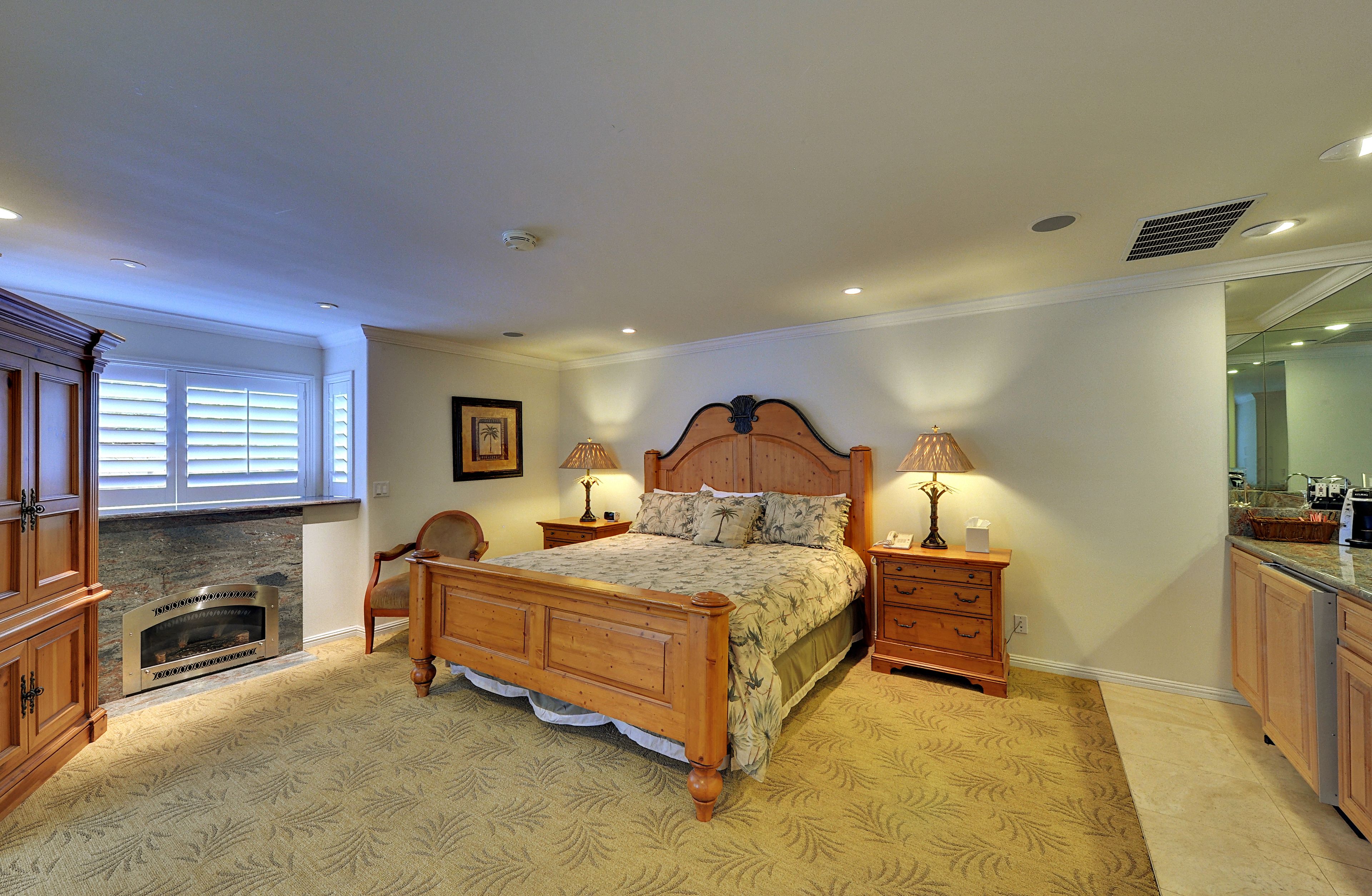 A bedroom with a bed, nightstands, a lamp, a fireplace, and wooden cabinets.
