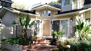 Une maison à deux étages avec un porche à l’avant, une entrée en briques et un petit jardin agrémenté de diverses plantes et fleurs.