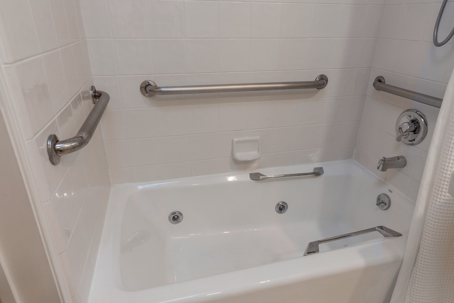 A white bathtub with grab bars, a soap dish, and a showerhead.