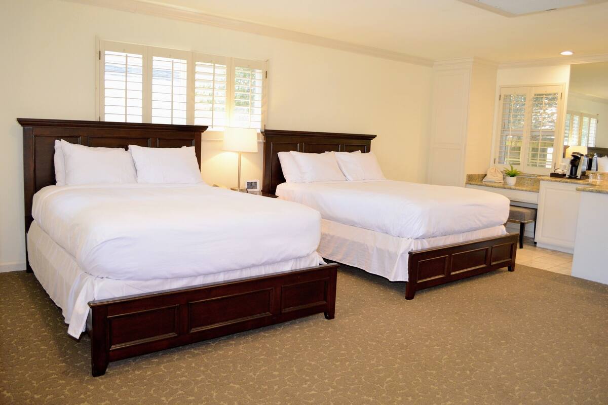 Une chambre d’hôtel avec deux lits doubles, un petit bureau avec une chaise et une fenêtre avec des stores.