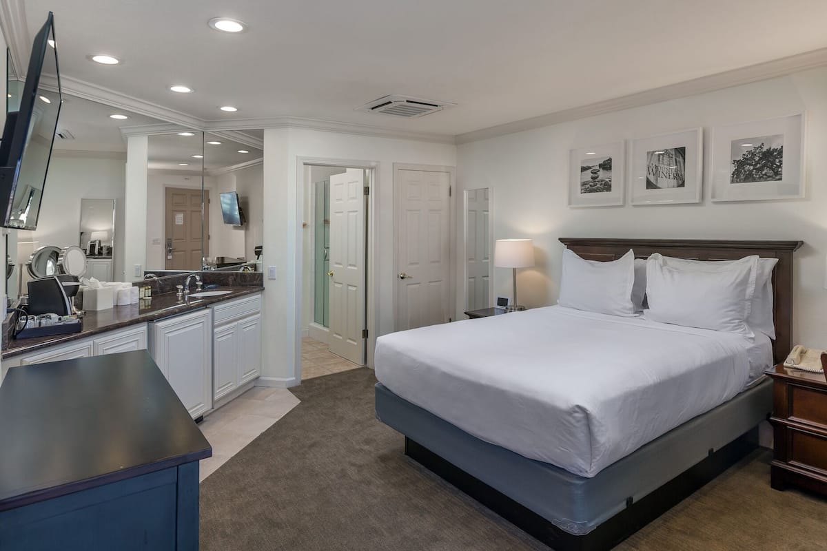 Une chambre d’hôtel avec un lit, une table de chevet, une lampe et un grand miroir.