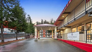 A hotel entrance with a covered parking area, a red and white building facade, and a sign indicating the hotel's name.
