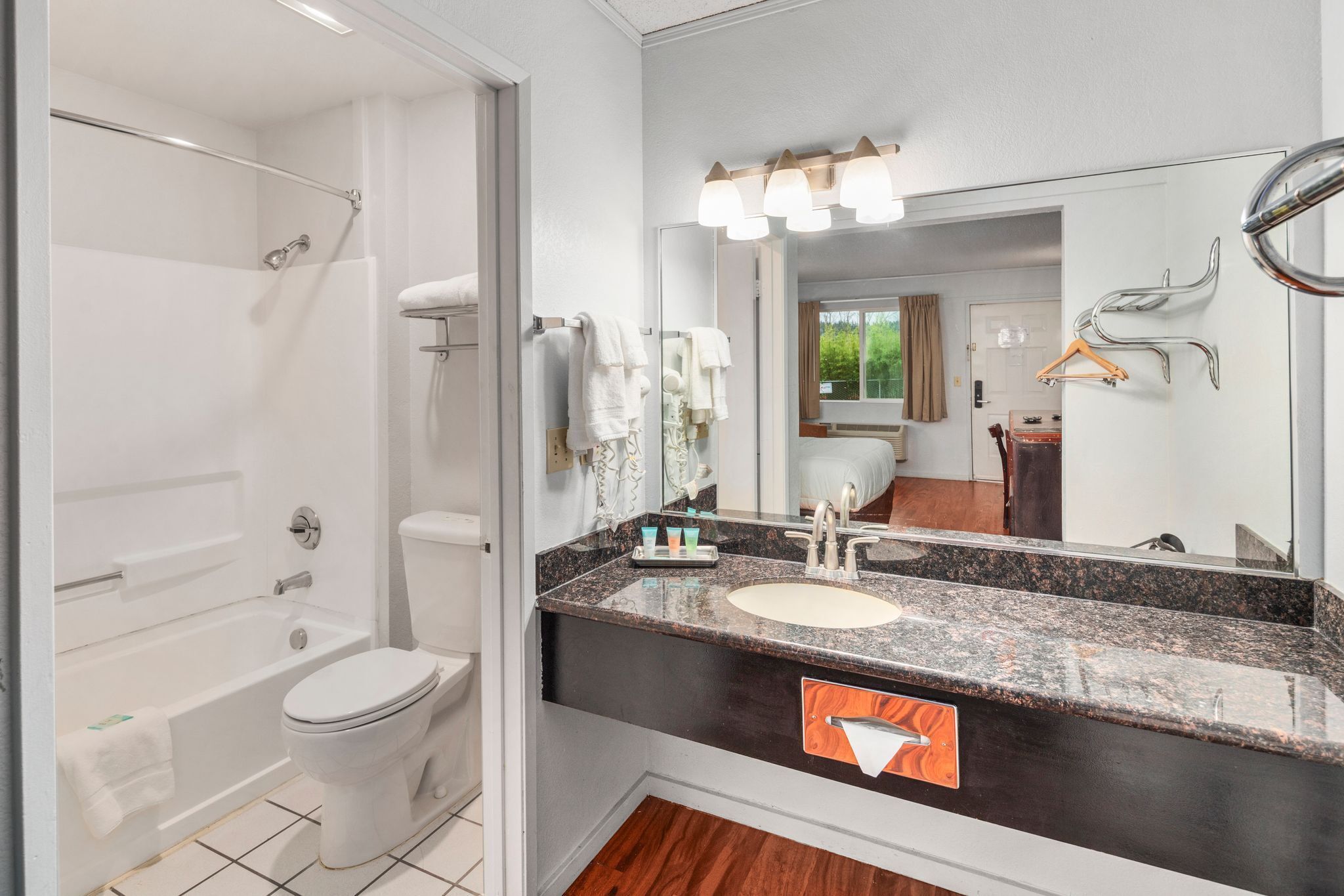 A modern bathroom with a white toilet, a bathtub, a sink with a granite countertop, and a mirror with lights.