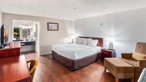 A hotel room with a large bed, a desk, a chair, a sofa, and a small table.