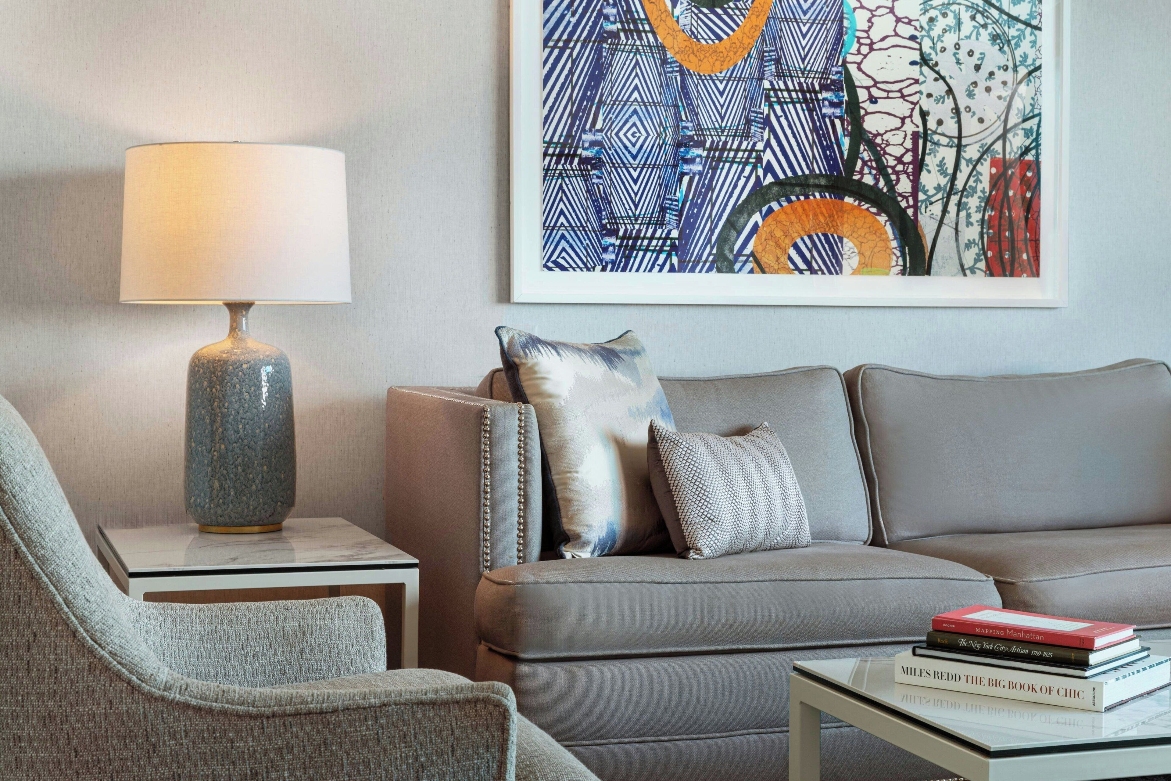 Un salon moderne avec un canapé, une table d’appoint sur laquelle se trouve une lampe, une œuvre d’art encadrée accrochée au mur et une pile de livres posée sur une petite table.