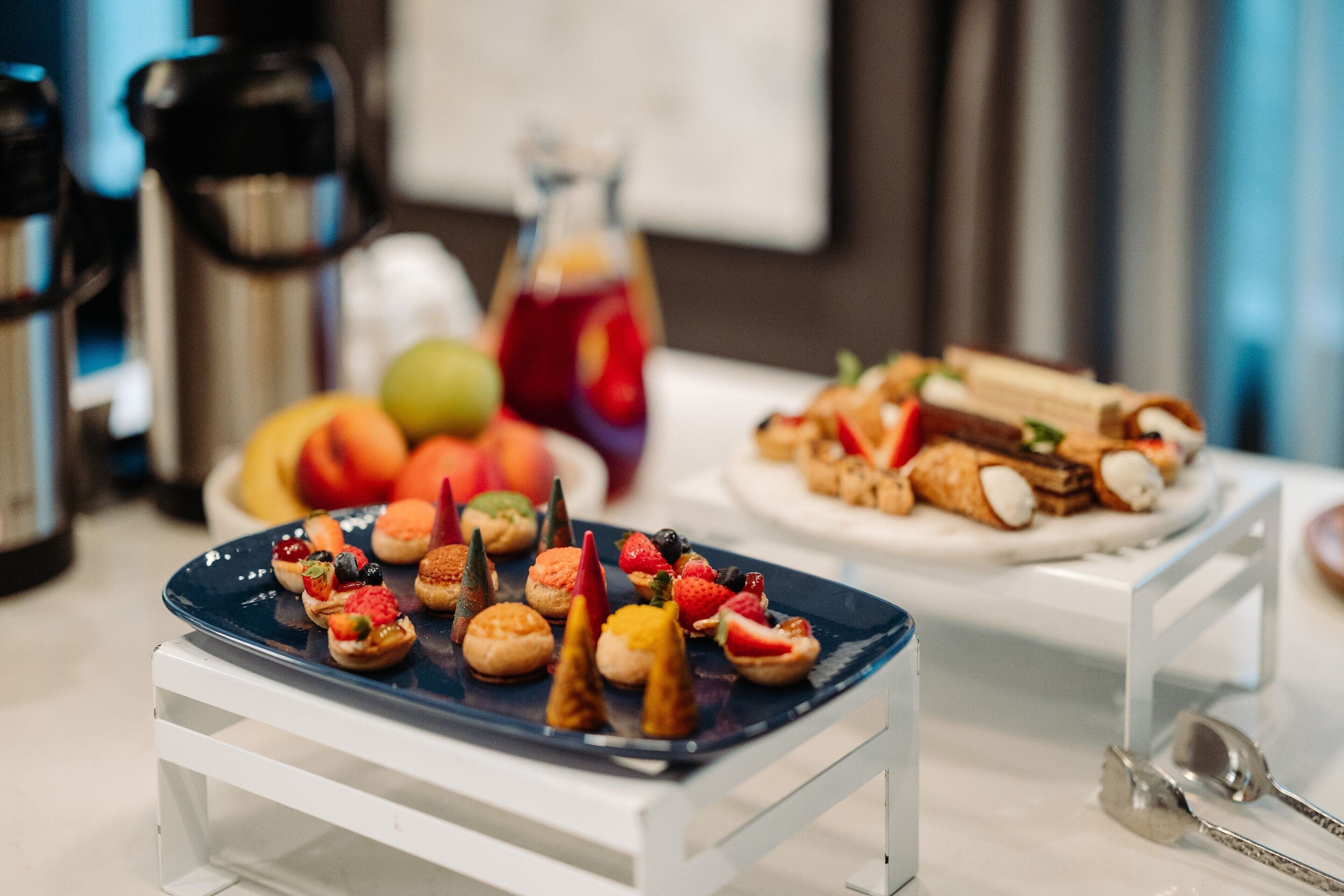 Una mesa con distintos alimentos, entre ellos pasteles y frutas, dispuestos en un plato azul y uno blanco.
