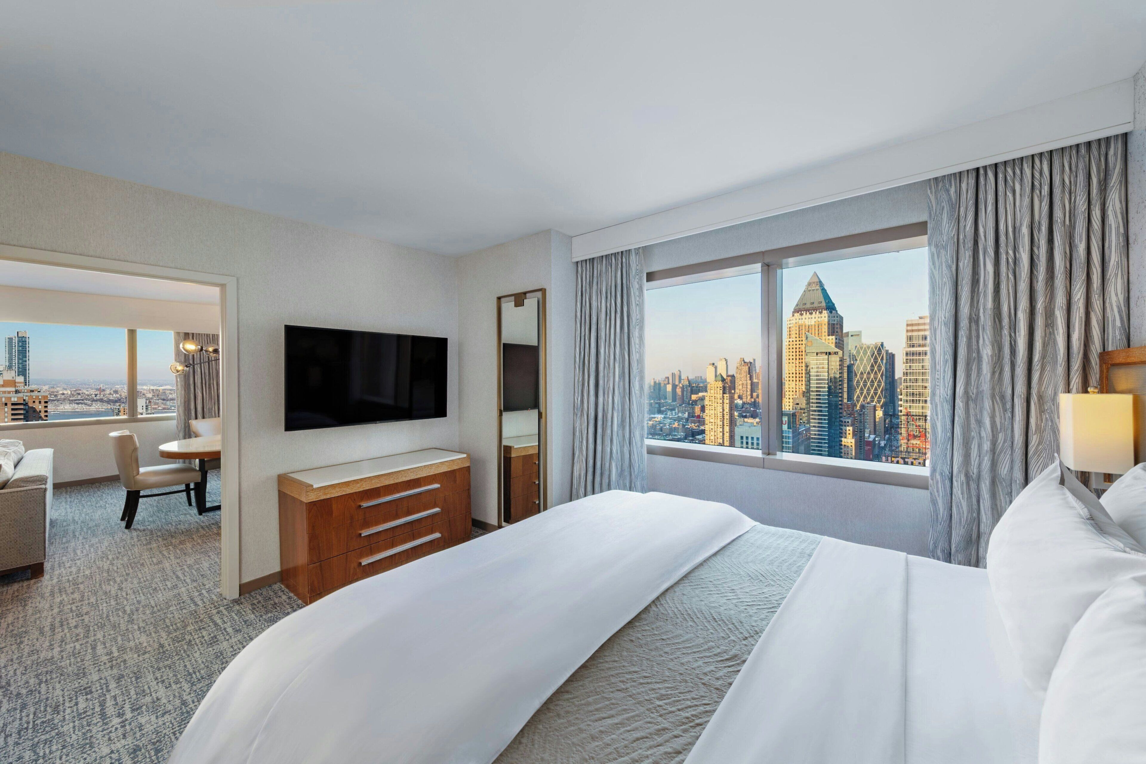 A hotel room with a bed, a TV, a desk, and a view of a city skyline.