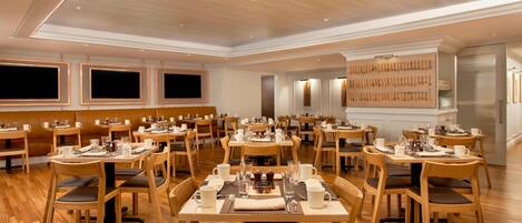 A spacious dining area with multiple tables and chairs, wooden flooring, and recessed lighting.
