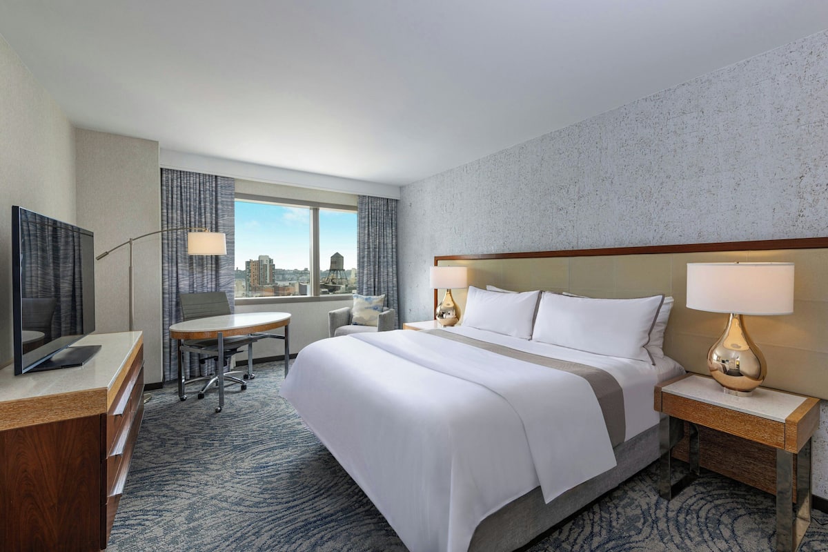 Een hotelkamer met een groot bed, een bureau, een televisie en uitzicht op de stad.