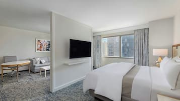 Habitación de hotel con cama, televisión montada en la pared, escritorio con silla y ventana con cortinas.