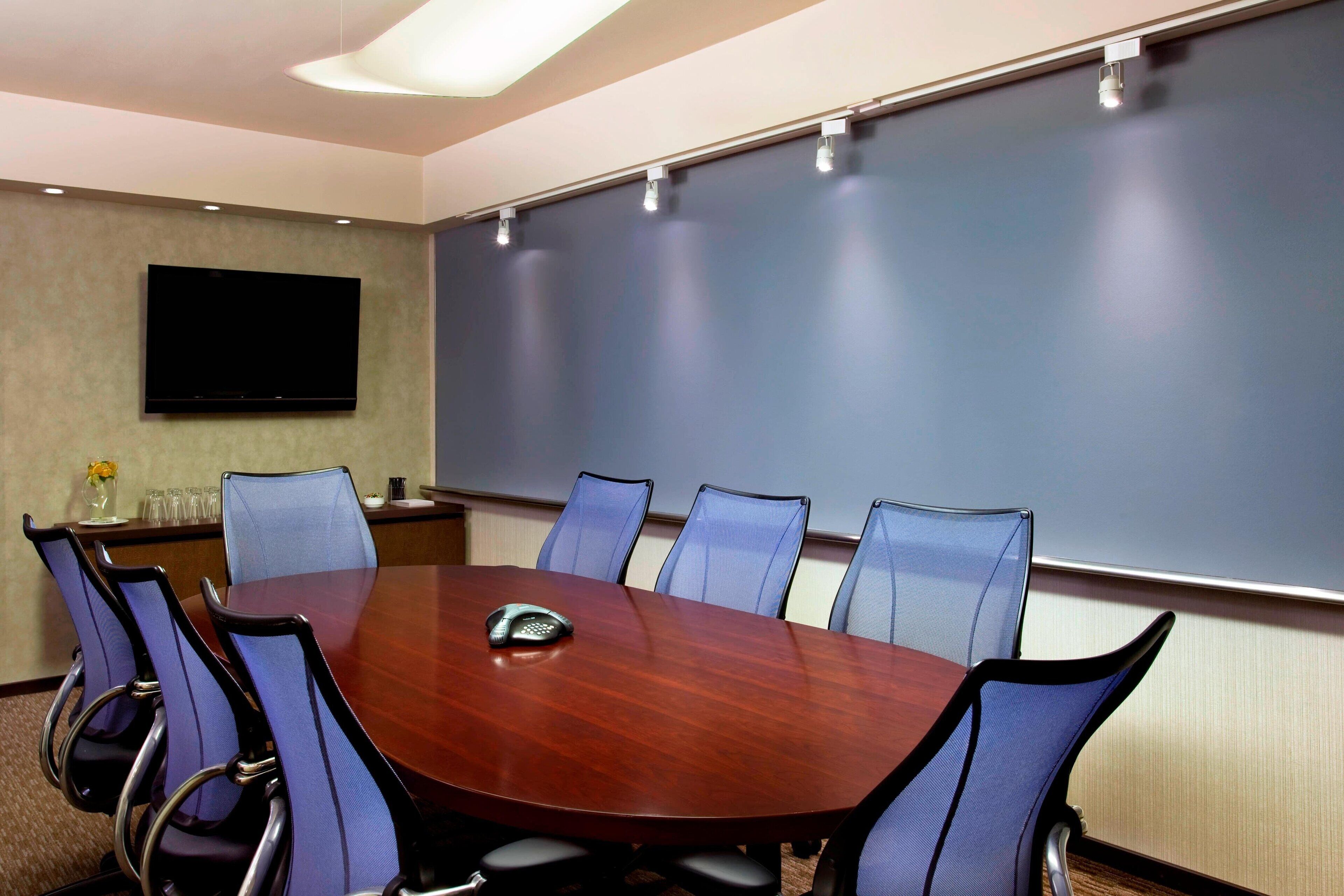 A conference room with a large table, six chairs, a projector screen, and a flat-screen TV.