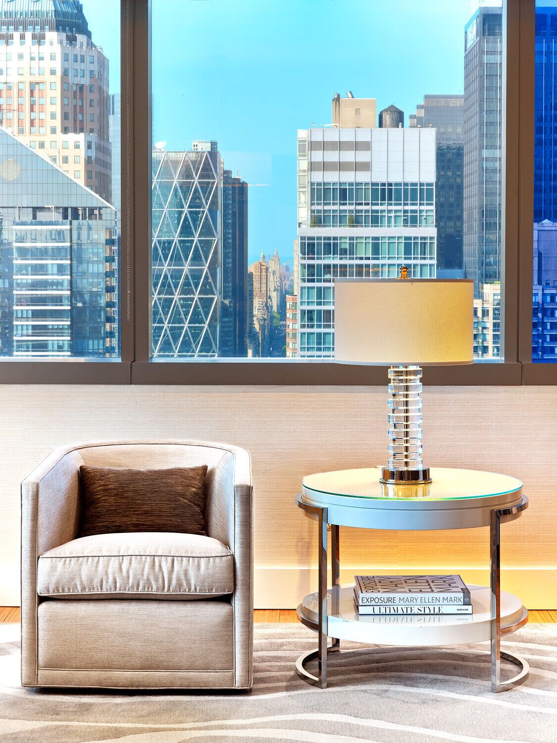 A modern room with a city view, a leather armchair, a glass table with a book, and a window with blinds.