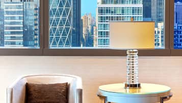 A modern room with a city view, a leather armchair, a glass table with a book, and a window with blinds.