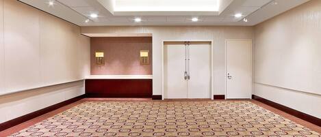 A spacious, well-lit conference room with patterned carpet, a reception area, and a door with a handle.