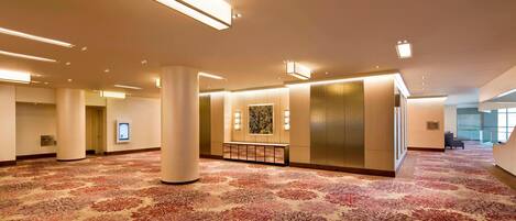 A spacious lobby with a patterned carpet, recessed lighting, and a reception area with a digital screen.