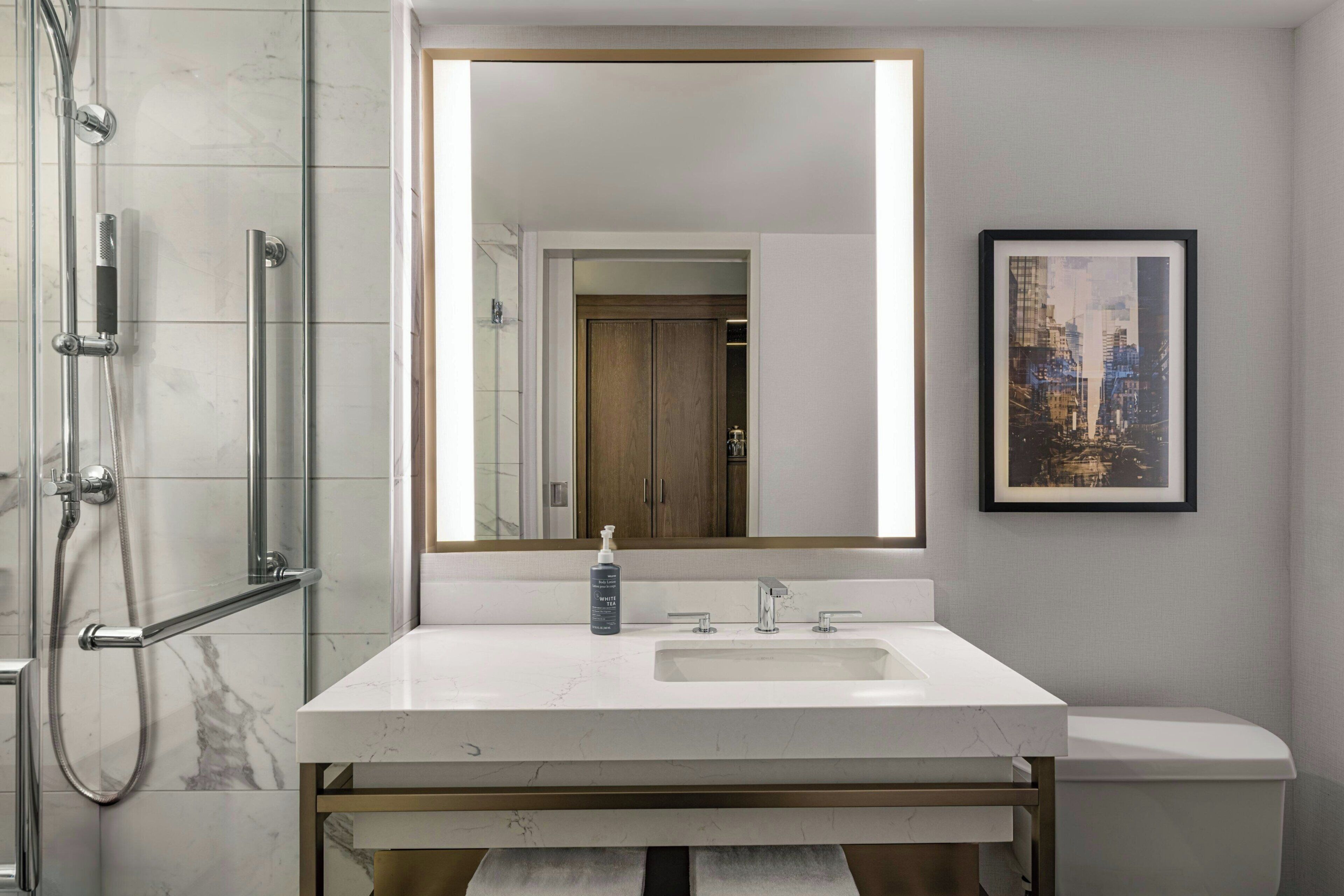 A bathroom with a large mirror, a sink, a shower, and a framed picture on the wall.