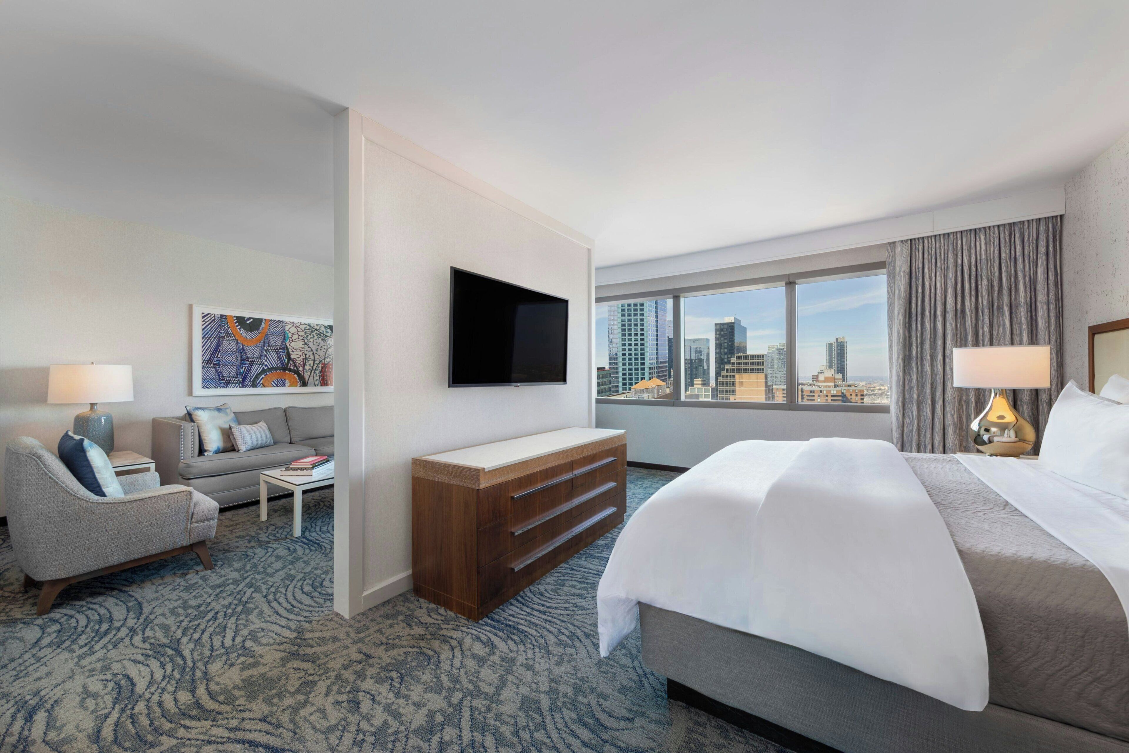 Une chambre d’hôtel comprenant un lit, un canapé, une télévision, un bureau et une grande fenêtre donnant sur la ville.