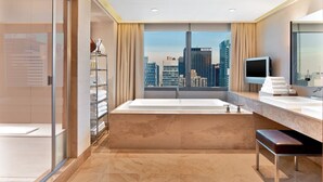 A modern bathroom with a bathtub, a large window with a city view, a vanity with a mirror, and a towel rack.