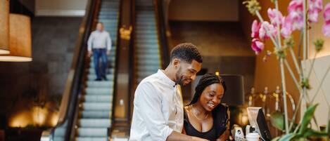 A man and woman standing at a reception desk in a modern lobby with an escalator in the background.