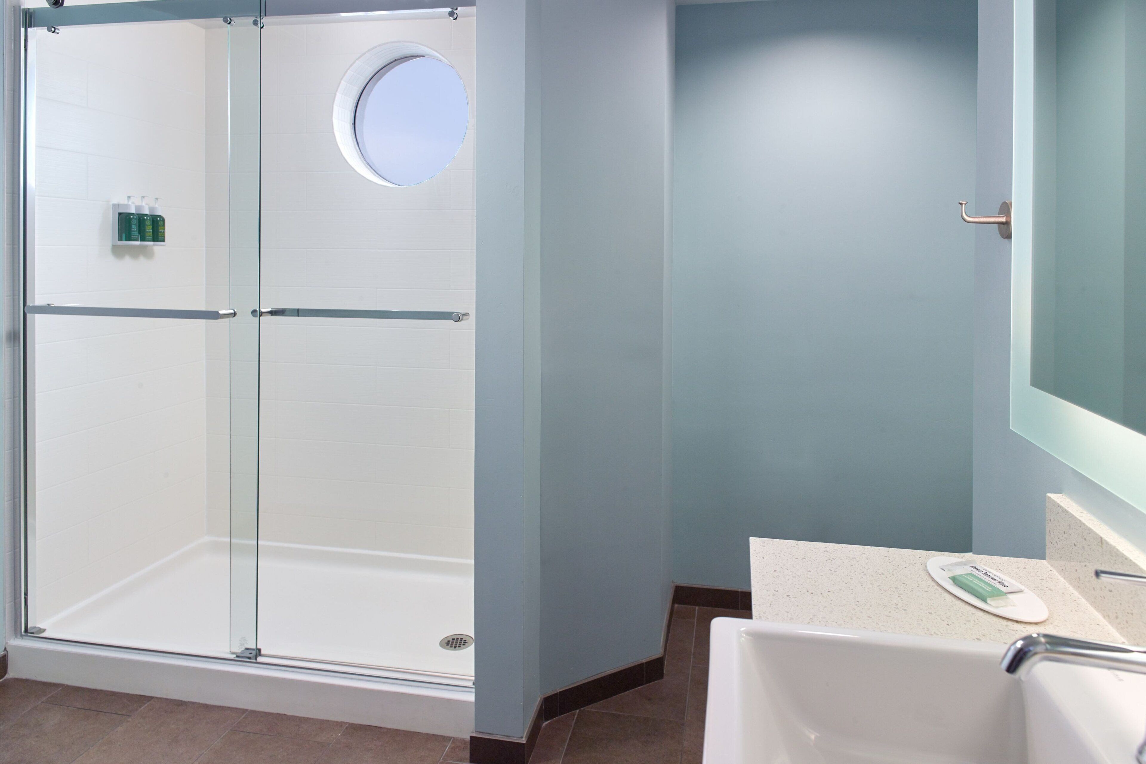 A modern bathroom with a glass-enclosed shower, a round mirror, and a white bathtub.
