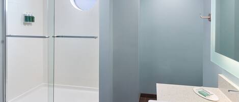 A modern bathroom with a glass-enclosed shower, a round mirror, and a white bathtub.
