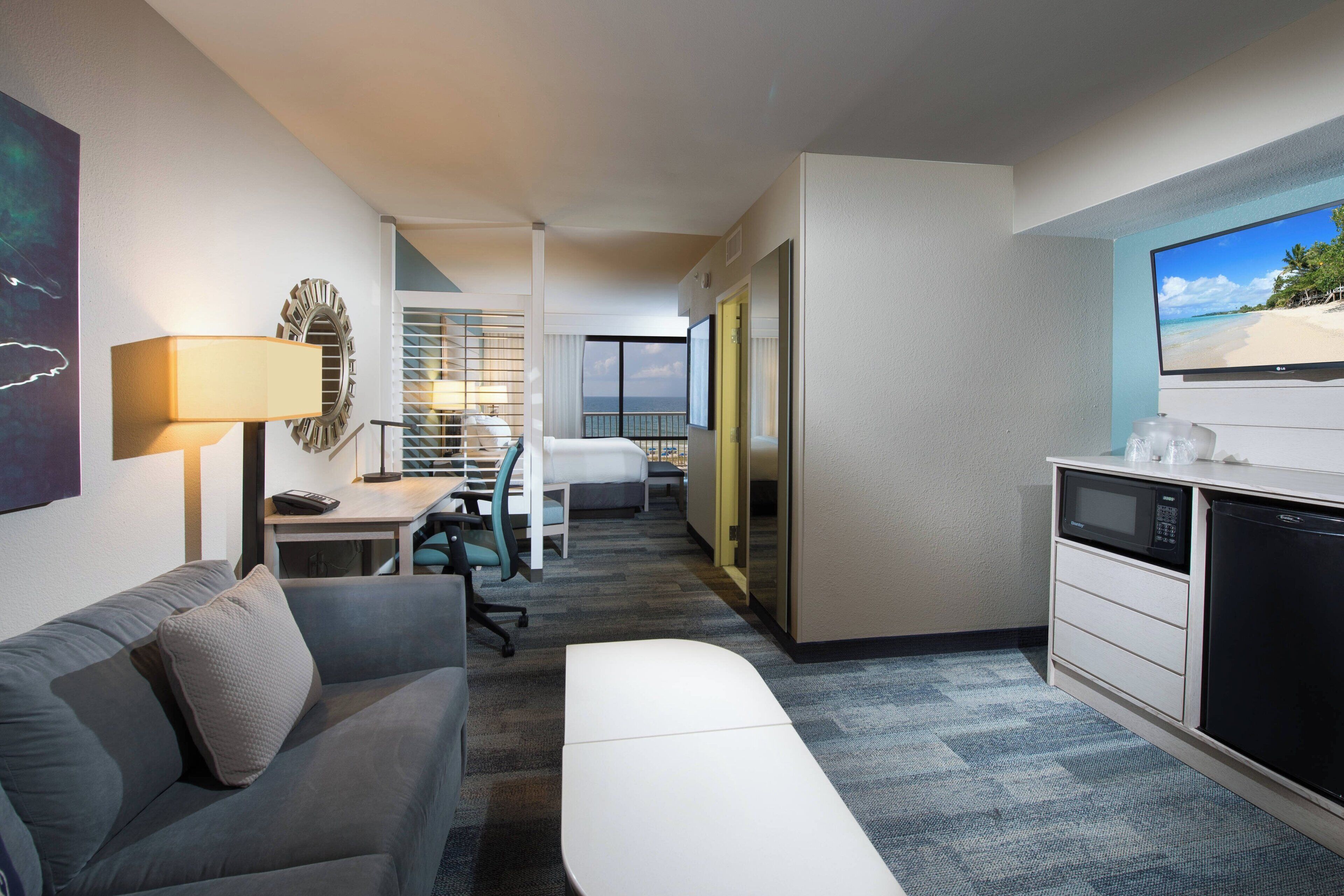 A hotel room with a sofa, a desk, a television, and a microwave.