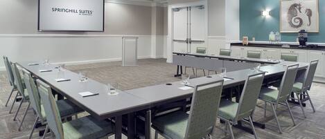 A conference room with a long table, chairs, a projector screen, and a whiteboard.
