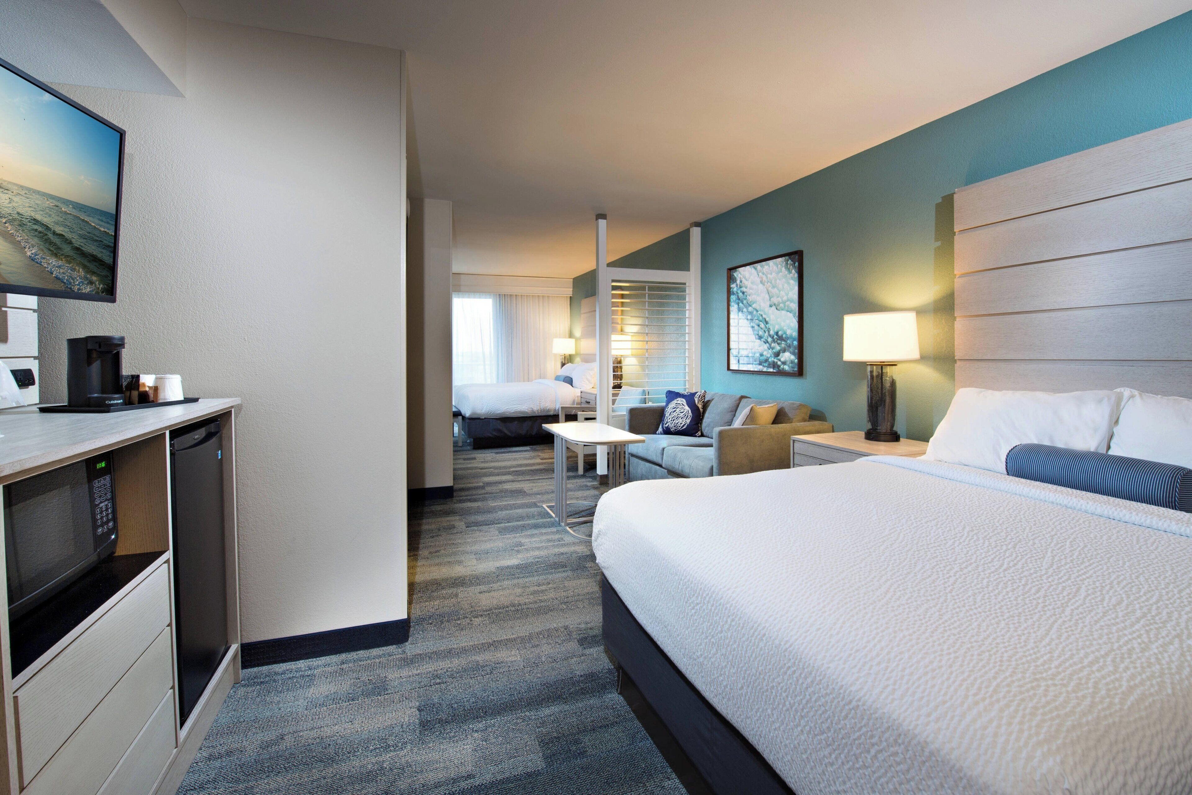A hotel room with a large bed, a desk with a coffee maker, a TV, and a view of the ocean.