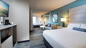 A hotel room with a large bed, a desk with a coffee maker, a TV, and a view of the ocean.